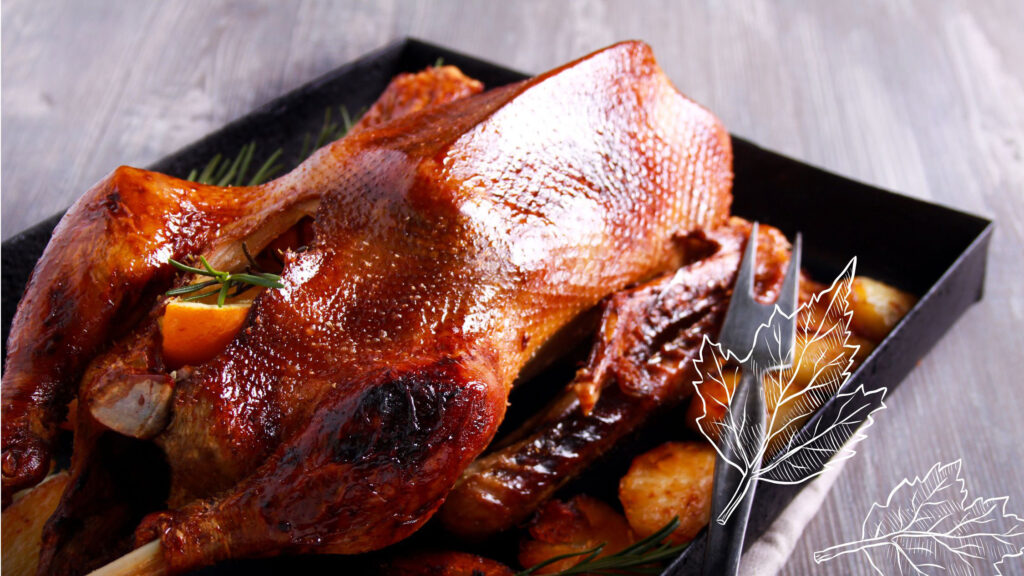 Eine knusprig gebratene Gans liegt in einer schwarzen Bratform, umgeben von gebräunten Kartoffeln und frischen Kräutern wie Rosmarin. Die goldbraune Haut glänzt appetitlich, eine Fleischgabel steckt seitlich im Braten. Im Vordergrund sind dekorative, eingezeichnete Herbstblätter zu sehen – ein Bild, das das saisonale Post-Martinstagsmenü des Schmidt’s Restaurant Dresden hervorhebt, zubereitet mit regionalen und nachhaltig ausgewählten Zutaten.