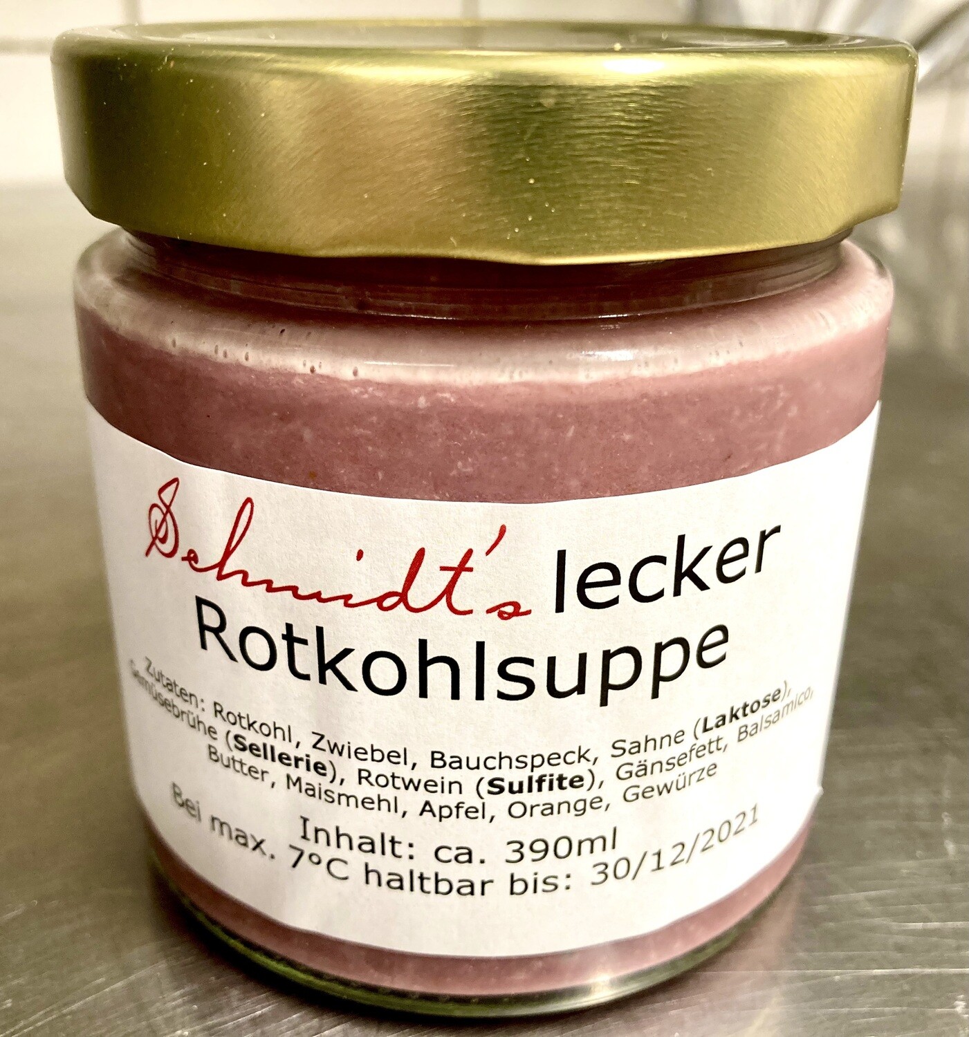 Ein Glas mit goldfarbenem Schraubdeckel und dem Etikett „Schmidt’s lecker Rotkohlsuppe“ steht auf einer Edelstahlfläche; das rosa-rote Süppchen ist durch das Glas sichtbar – ein Produkt aus dem Shop des Schmidt’s Restaurant Dresden.