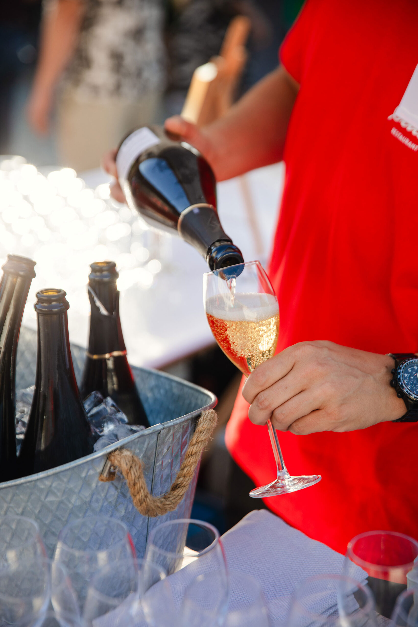 Ein Catering-Mitarbeiter von Schmidts füllt allen Gästen ein Glas Champagner ein.